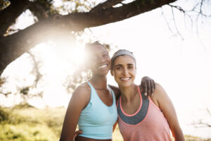 interracial women portrait friends with hug nature fitness workout outdoor hiking by tree young female people smile with embrace support trust exercise training together